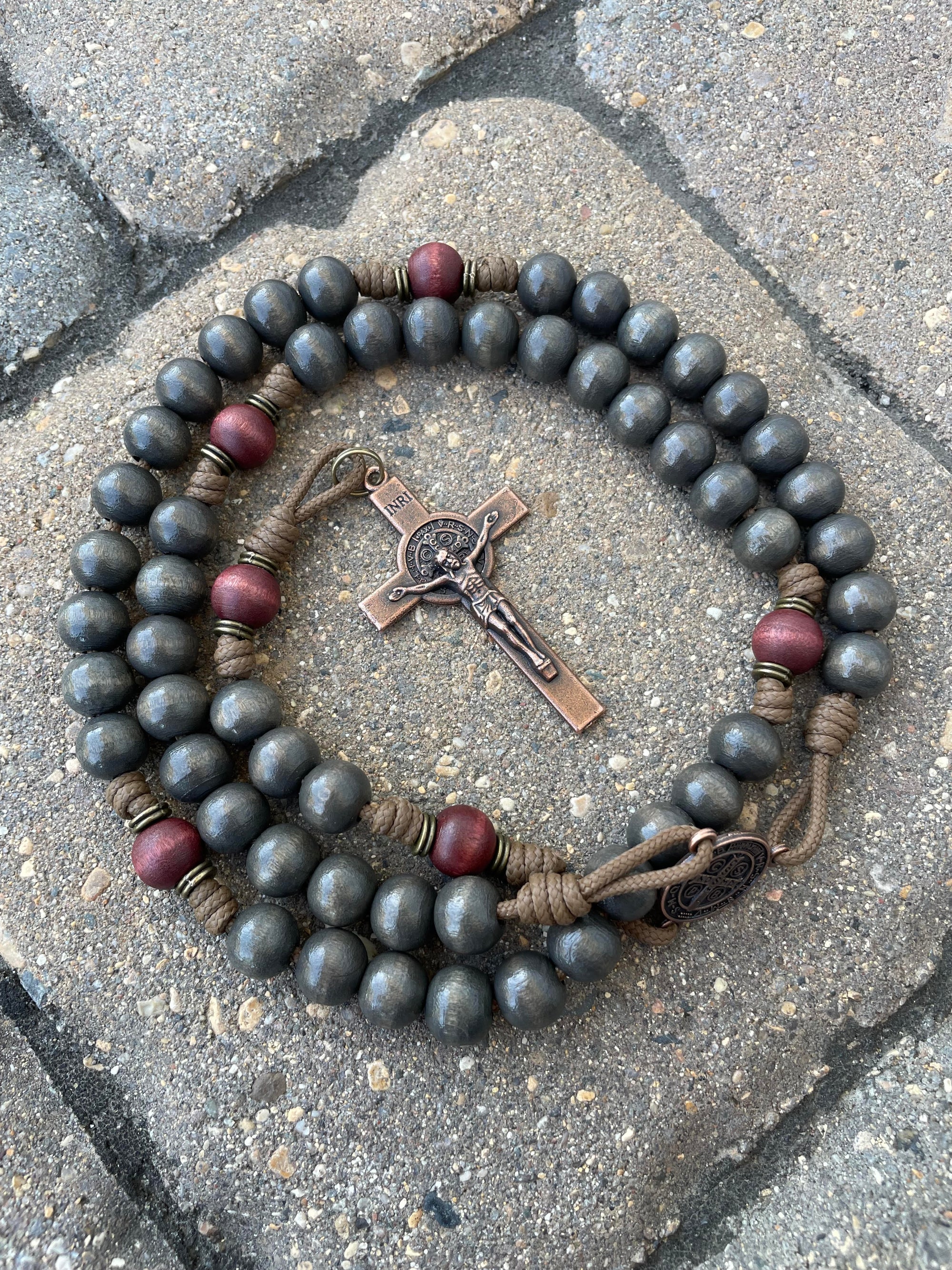 A Logos catholic rosary with black and red wooden beads and a crucifix pendant on stone pavers