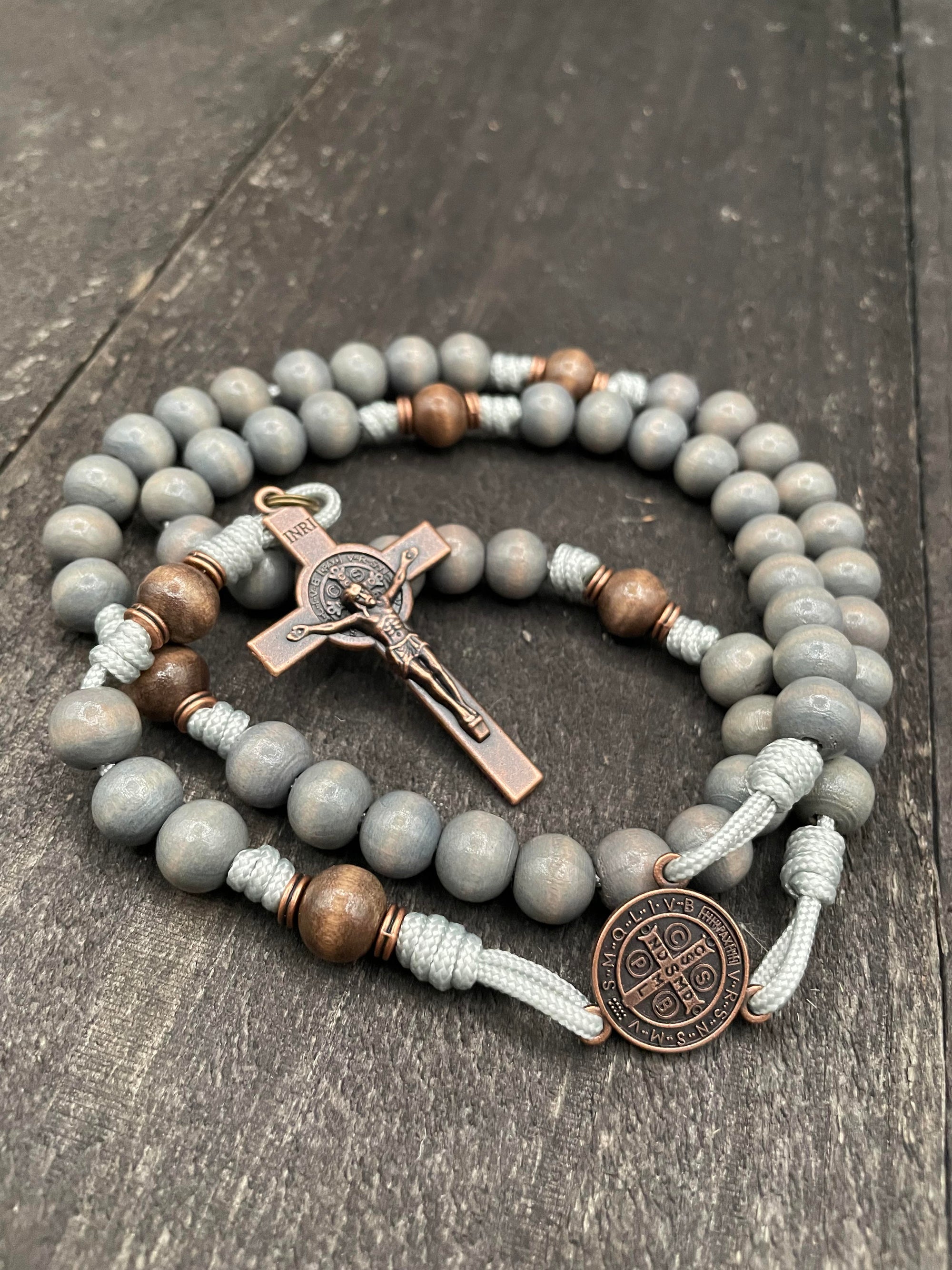 Handcrafted Catholic rosary with polished silver beads, an ornate crucifix, and a detailed centerpiece, displayed on a smooth white surface.